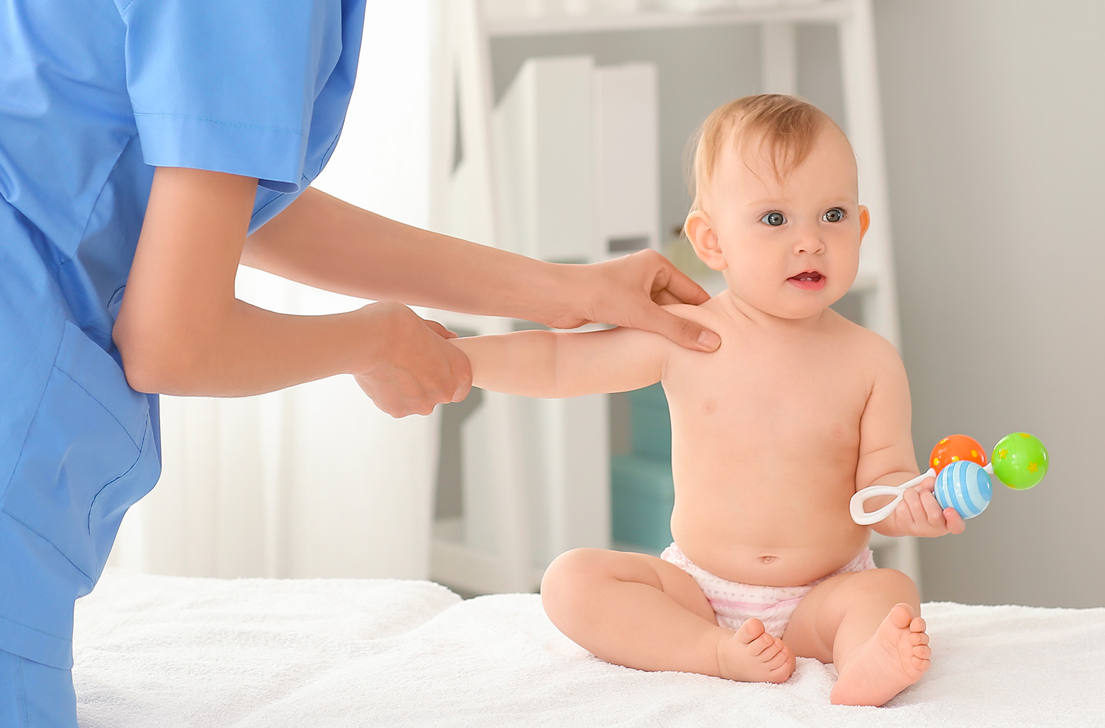 Jolie photo d un bebe avec un jouet a la main se fait examiner par une kinesitherapeute pediatrie traitement | IK Paris