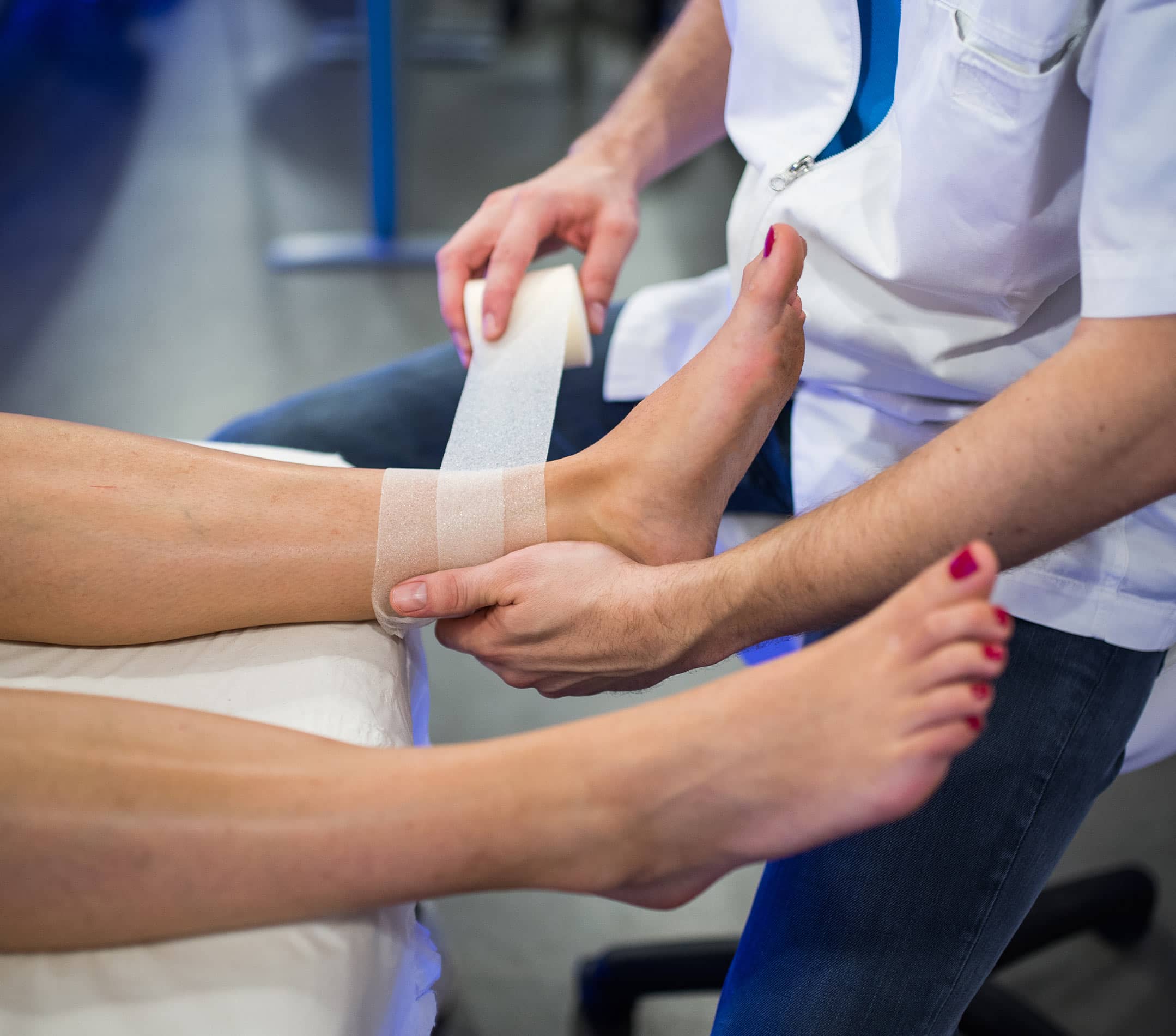 Photo des pieds d une femme se faisant un bandage de la part d un kinesitherapeute - ecoute traitement suivi| IK Paris