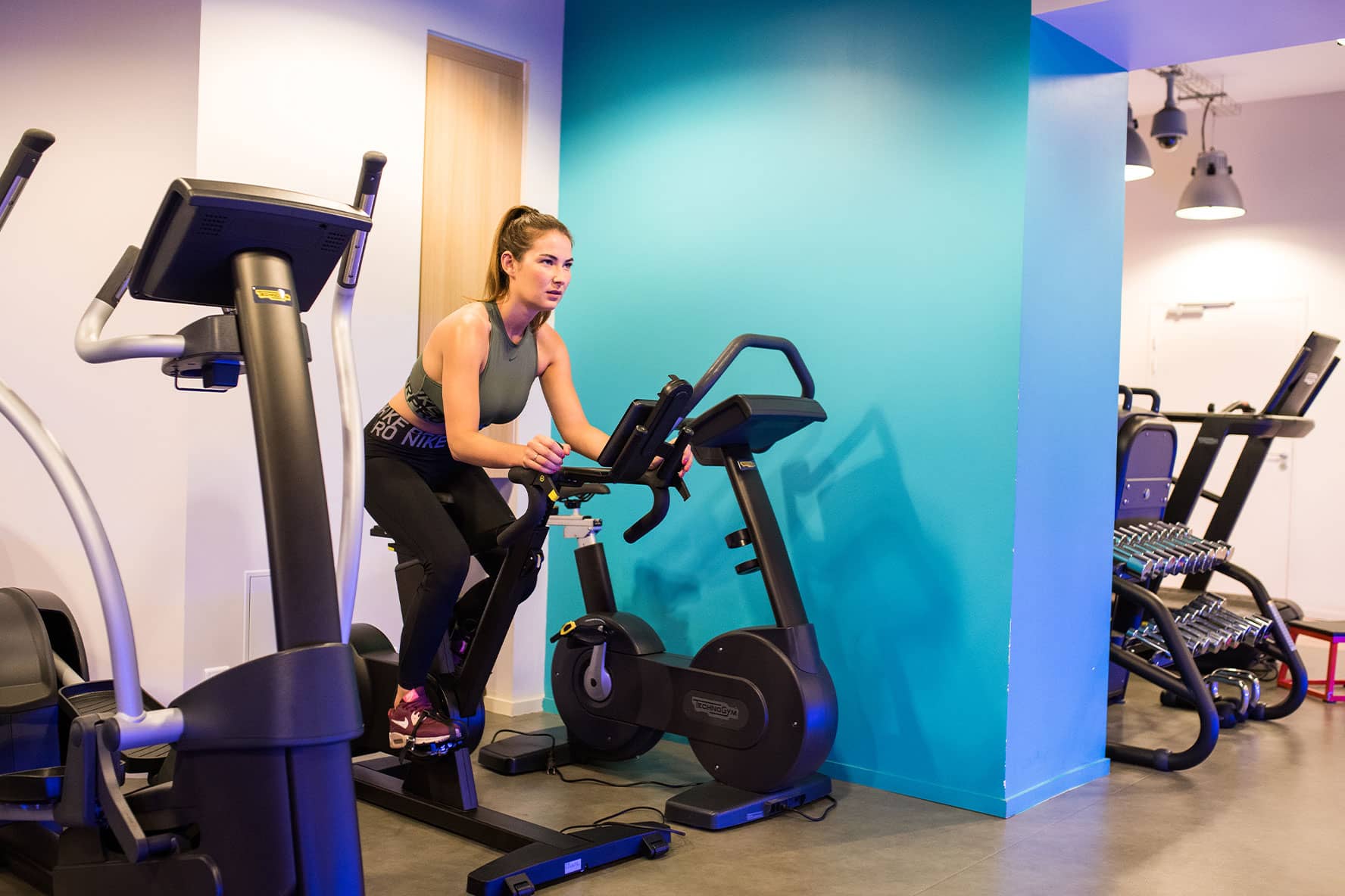 Jeune femme faisant des exercices sur un velo de salle de sport - high tech | IK Paris