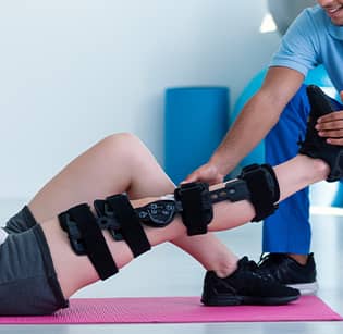 Jeune homme allongee et un kinesitherapeute qui l aide a faire des etirement pour sa jambe - les pathologies liees au sport | IK Paris